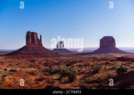 Berühmte butte Formationen mit rotem Felsen in Monument Valley während der Dämmerung dunkle Nacht in Arizona mit Mond Mondlicht blauen Stunde Himmel Panoramablick Stockfoto