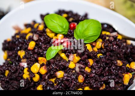 Makro Nahaufnahme Textur von verbotenen chinesischen schwarzen Reis Gericht mit Mais, Gemüse Basilikum Blätter Dekoration auf Teller Schüssel isoliert Stockfoto