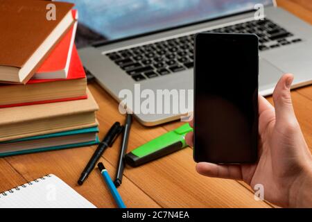 Männliche Hand hält ein Telefon. Notebooks, Bücher und Büroprodukte Stockfoto