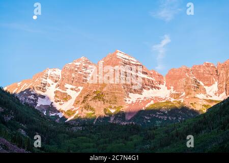 Maroon Bells Gipfel Nahaufnahme mit Sonnenlicht und Schatten mit Mond in Aspen, Colorado blauen Himmel felsigen Bergen und Schnee im Juli 2019 Sommer in der Dämmerung Stockfoto