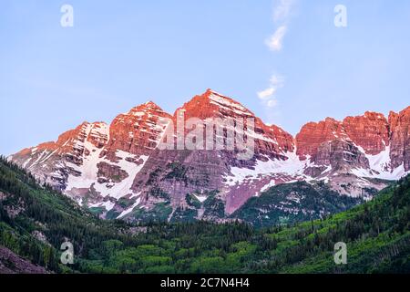 Maroon Bells Gipfel Nahaufnahme mit Sonnenlicht in Aspen, Colorado zur blauen Stunde mit felsigen Bergen und Schnee im Juli 2019 Sommer bei Sonnenaufgang mit violettem Sattel Stockfoto