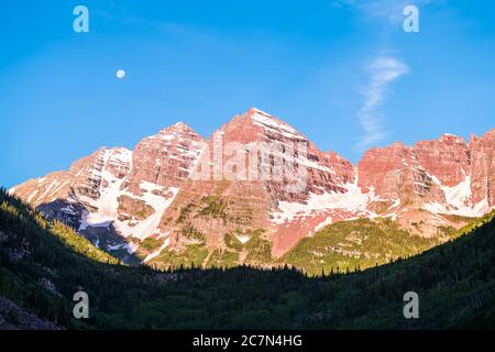 Kastanienbraune Glocken Gipfel Nahaufnahme mit Sonnenlicht und Schatten mit Mond in Aspen, Colorado blauen Himmel felsigen Bergen und Schnee im Juli 2019 Sommer bei Sonnenaufgang Stockfoto