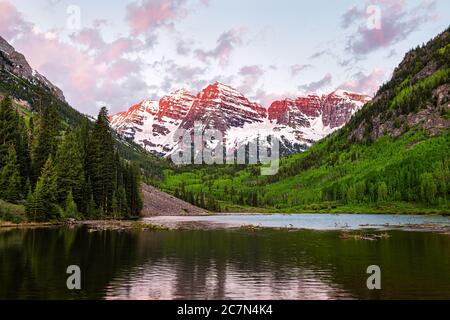 Kastanienbraune Glocken in Aspen, Colorado mit Wolken bei Sonnenaufgang und felsigen Berggipfel See Reflexion im Sommer mit rotem Sonnenlicht und grünen Waldbäumen Stockfoto