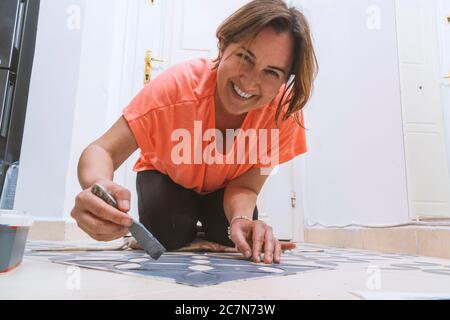 Zu Hause bleiben und Heimwerker-Konzept: Junge kaukasische Frau mit orangefarbenem T-Shirt malt Fliesen von ihrem Haus. Stockfoto