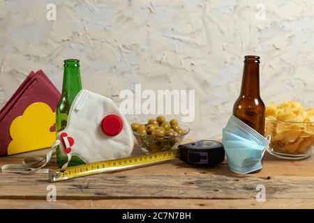 Bierflaschen mit medizinischen Masken bedeckt neben Oliven, Chips und Maßband auf dem Tisch Stockfoto