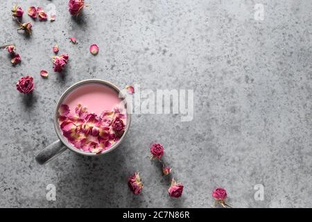 Rose Mond Milch in grauer Tasse und Rosenblätter auf grauem Hintergrund. Draufsicht. Speicherplatz kopieren Stockfoto