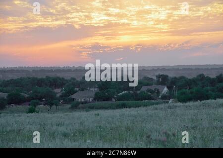 Die ländliche Landschaft im Sommer ist in den Strahlen des Sonnenuntergangs und von bewölktem Himmel beleuchtet. Stockfoto