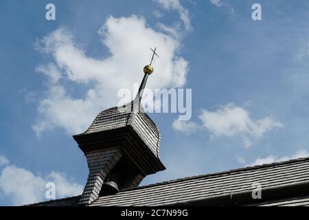 Ein alter Glockenturm auf einer Dorfkirche mit einem Kreuz auf der Spitze. Der Glockenturm und das Dach sind mit Holzschindeln bedeckt. Stockfoto