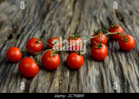 Reife frische Kirschtomaten auf Ast auf einem alten Holztisch. Selektiver Fokus. Stockfoto