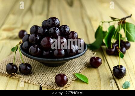 Frische Sauerkirschen in einer schwarzen Schüssel und grüne Blätter auf dem Holztisch. Frische reife Sauerkirschen. Selektiver Fokus. Stockfoto