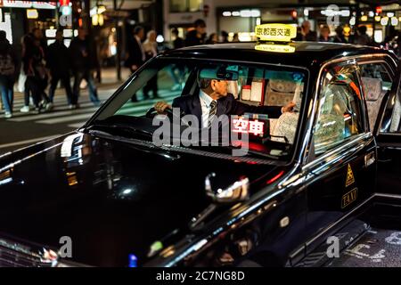 Kyoto, Japan - 9. April 2019: Gion Straße mit beleuchteten Gebäuden bunte Bokeh Nacht und schwarz Taxi im Verkehr mit Fahrer im Inneren Stockfoto