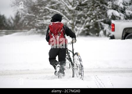 Ein Radfahrer mit Rucksack schiebt sein Fahrrad während eines seltenen Schneesturms an der Westküste im Vorort View Royal in Victoria, Großbritannien, durch den Schnee Stockfoto
