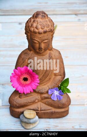 Kleine Statue von Buddha auf dem Tisch mit einem Transvaal daisy und eine größere periwinkle Stockfoto