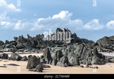 Schwarze dunkle Felsbrocken liegen an einem Strand nach der Küste in Axim Ghana Westafrika Stockfoto