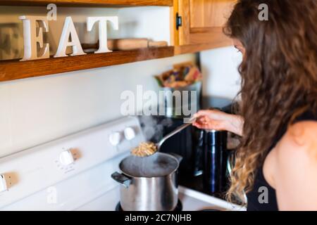 Junge Frau Kochen Pasta auf rustikalen Vintage Herd mit Edelstahl Topf und Dampf in Retro-Küche mit Eat-Zeichen Dekoration in Bauernhaus Cotta Stockfoto