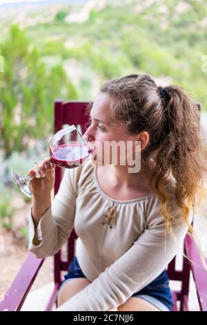 Frau sitzt draußen auf dem Stuhl trinken Glas Rotwein oder Preiselbeersaft in Santa Fe Desert Garten Hinterhof vertikale Ansicht Stockfoto