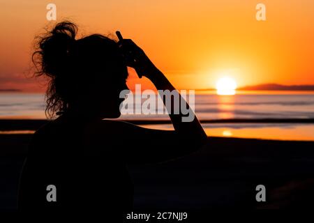 Frau mit der Hand auf der Stirn beobachten Sonnenpfad Reflexion Sonnenuntergang auf Great Salt Lake im Antelope Island State Park mit Wasseroberfläche und Silhouette Stockfoto