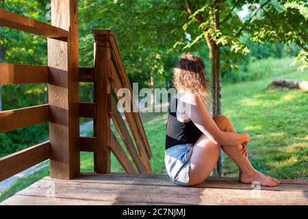 Sommerhaus Veranda mit Frau auf Stufen des Hauses im Hinterhof sitzen Morgen Holzhütte Blick auf die Aussicht in der Landschaft Stockfoto