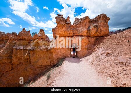 Junge Frau, die im Tunnel-Bogen der Wüstenlandschaft im Bryce Canyon National Park auf der Navajo Loop Queen's Garden Trail mit Sandsteinfelsen steht Stockfoto