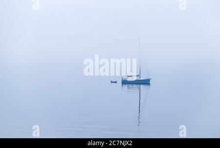 Ein einsames Segelboot sitzt im nebelbedeckten Wasser. Stockfoto