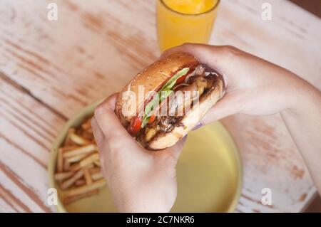 Selektive Aufnahme einer Person, die einen leckeren Hamburger hält Mit Pommes auf dem Tisch Stockfoto