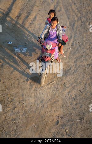 Ein Blick von oben auf eine Frau und ihr Kind, die auf einer unbefestigten Straße in Mandalay, Myanmar, mit dem Motorrad fahren Stockfoto