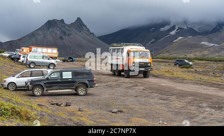 Viele SUVs und Personenkraftwagen fahren und parken entlang der Bergstraße am Fuße des Vulkans bei dramatischem bewölktem Wetter, vulkanische Landschaft Stockfoto