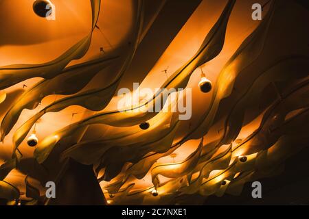 Abstrakte wellenförmige gelbe Deckendekoration mit kreisförmigen Leuchten Stockfoto