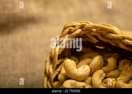 Cashewnüsse in einem Korbkorb auf Sackleinen mit einer rauen Oberflächenstruktur. Nahaufnahme Stockfoto