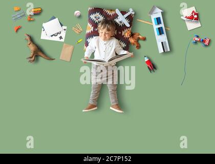 Kleiner Junge lügt und liest ein Buch unter seinen Spielsachen Stockfoto