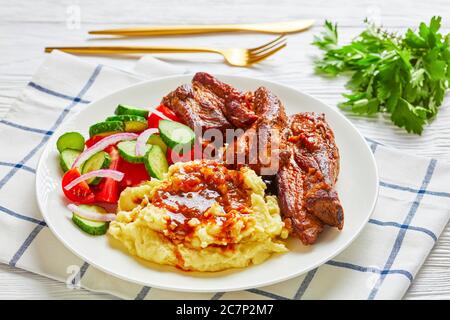 Restaurant Mahlzeit: Kartoffelpüree mit geschmorten Schweinefleisch Rippchen, braune Sauce, Salat von gehackten Tomaten, Gurken, rote Zwiebeln, Petersilie auf einem weißen Teller mit Stockfoto