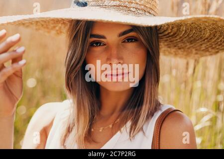 Schöne Frau in Strohhut posiert auf einem Feld und Blick auf die Kamera Stockfoto