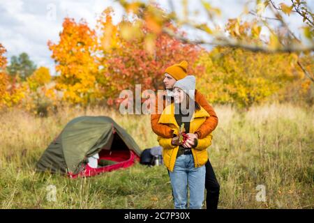 Reise, Liebe und Herbstkonzept - junges verliebtes Paar posiert in der Nähe von grünem Zelt im Herbstwald Stockfoto