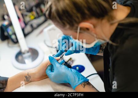 Nahaufnahme der Kosmetikerin, die die Nägel ihrer Kundin mit blauem und gelbem Nagellack malt. Stockfoto