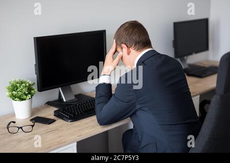 Rückansicht des jungen gestressten Geschäftsmanns im Büro - leerer pc-Bildschirm mit Kopierraum Stockfoto