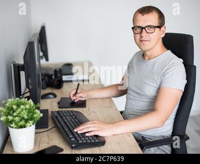 Portrait von jungen schönen männlichen Fotografen Bearbeitung von Bildern mit Computer im modernen Büro oder zu Hause Stockfoto