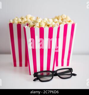 Kino- und Lebensmittelkonzept - Popcorn in rot gestreiften Schachteln und 3d-Brillen Stockfoto