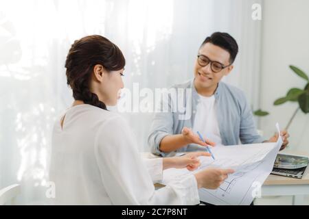 Architekt und Architektin diskutieren über eine Reihe von Blaupausen, die auf einem Tisch im Büro verteilt sind. Stockfoto