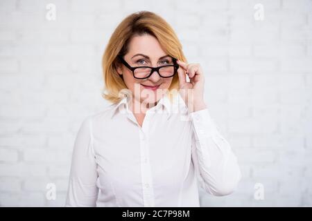 Porträt einer fröhlichen reifen Geschäftsfrau in Brillen posiert über weißen Ziegelwand Stockfoto