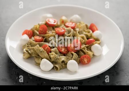 Fettuccine mit Pesto, Tomaten und Mozzarella auf weißem Teller Stockfoto