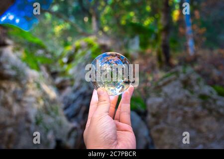 Nahaufnahme einer Kristallkugel in der Hand einer Person Spiegelt die umliegende Natur wider Stockfoto