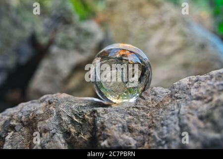 Nahaufnahme einer Kristallkugel auf einem reflektierenden Stein Umliegende Natur Stockfoto