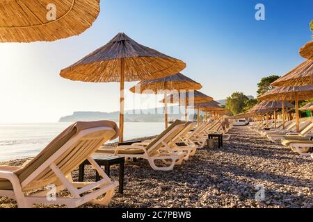Sonnenschirm und Liegestuhl am Strand bei Sonnenaufgang Stockfoto