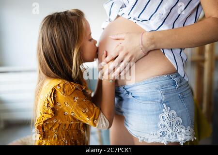 Glückliches Kind Mädchen umarmt Bauch der schwangeren Mutter Stockfoto