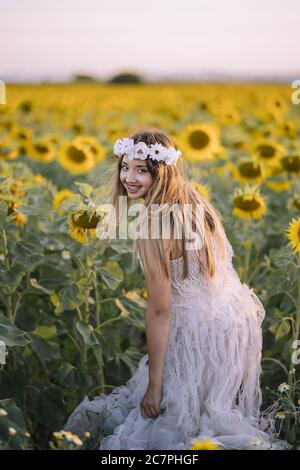 Schöne Frau in einem weißen Kleid, lächelnd und stehend im Sonnenblumenfeld Stockfoto