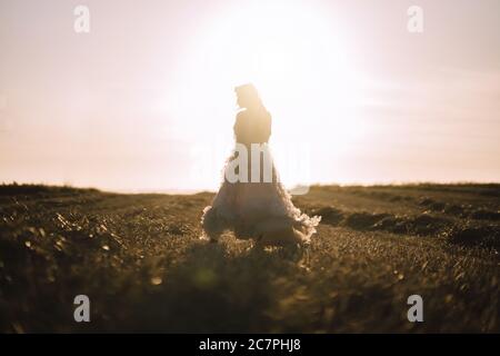 Frau in einem weißen Kleid, auf dem Feld zu gehen und unter den Sonnenstrahlen zu glänzen Stockfoto