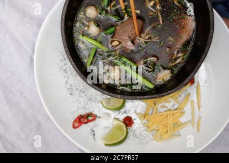 Traditionelle vietnamesische Pho bo Suppe mit Gemüse und Rindfleisch in schwarzer Schüssel auf weißem Teller Stockfoto