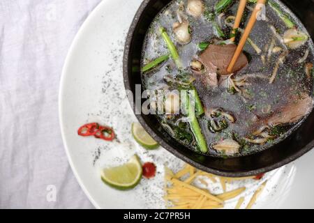 Traditionelle vietnamesische Pho bo Suppe mit Gemüse und Rindfleisch in schwarzer Schüssel auf weißem Teller Stockfoto