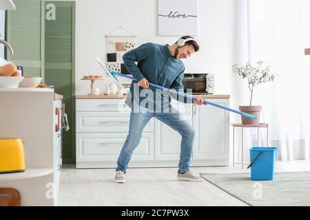 Schöner junger Mann, der Spaß hat, während er in der Küche Boden wischt Stockfoto