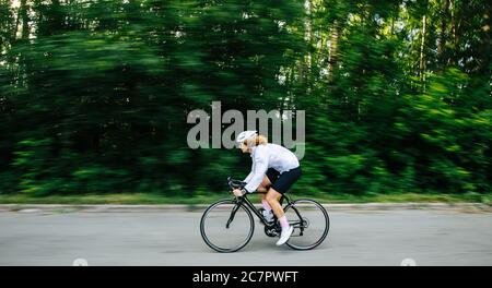 Seitenansicht der jungen athletischen Frau, die auf dem Profi-Fahrrad in einem weißen Helm fährt Stockfoto